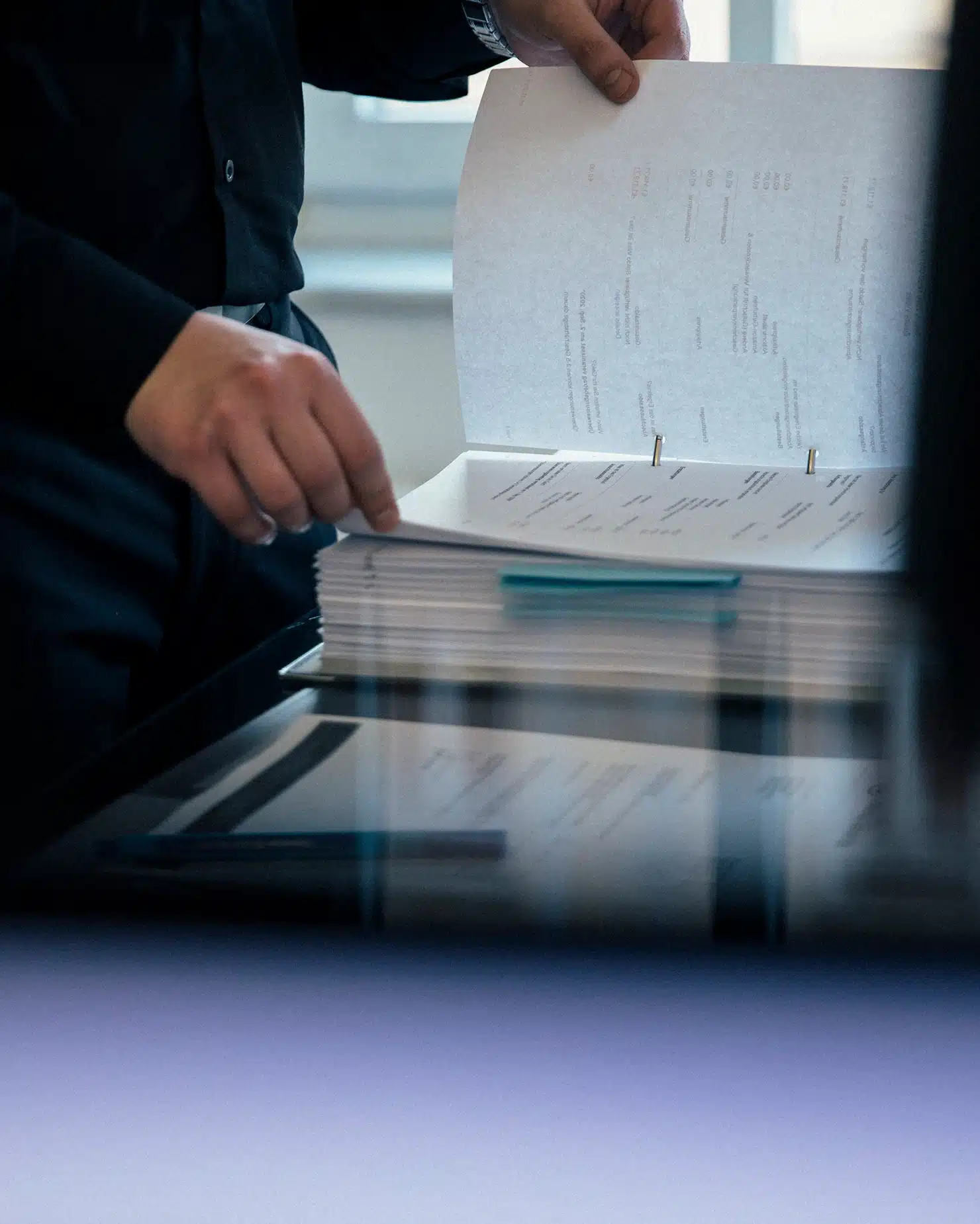 Nahaufnahme einer Person in dunkler Kleidung blättert im Ringordner; blaugrüne Trennfolie sichtbar.